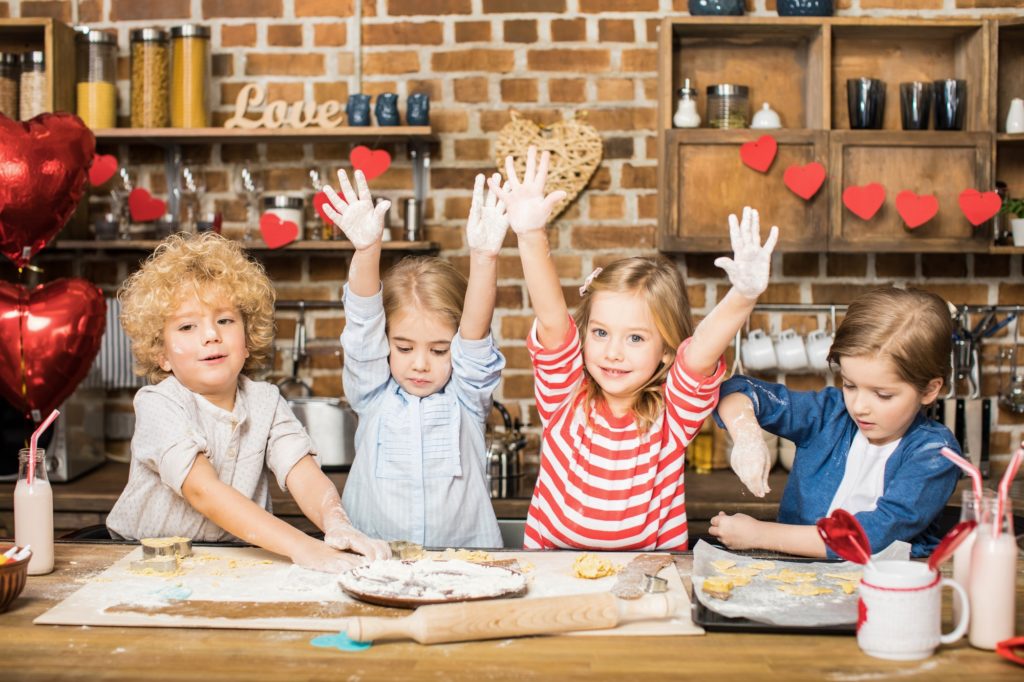 Four cute little children cooking biscuits and showing hands in flour